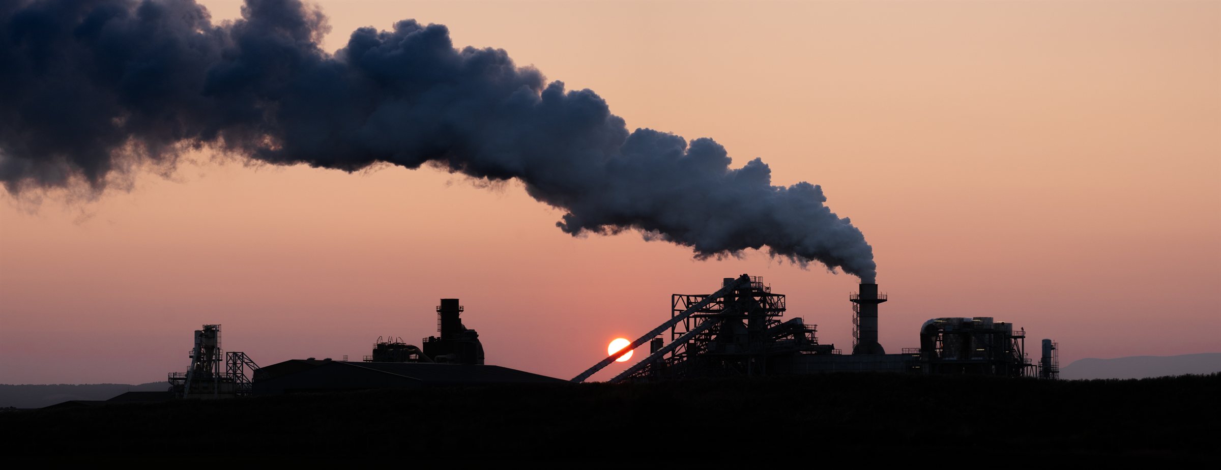 A plume of smoke from a works against a pink sunset