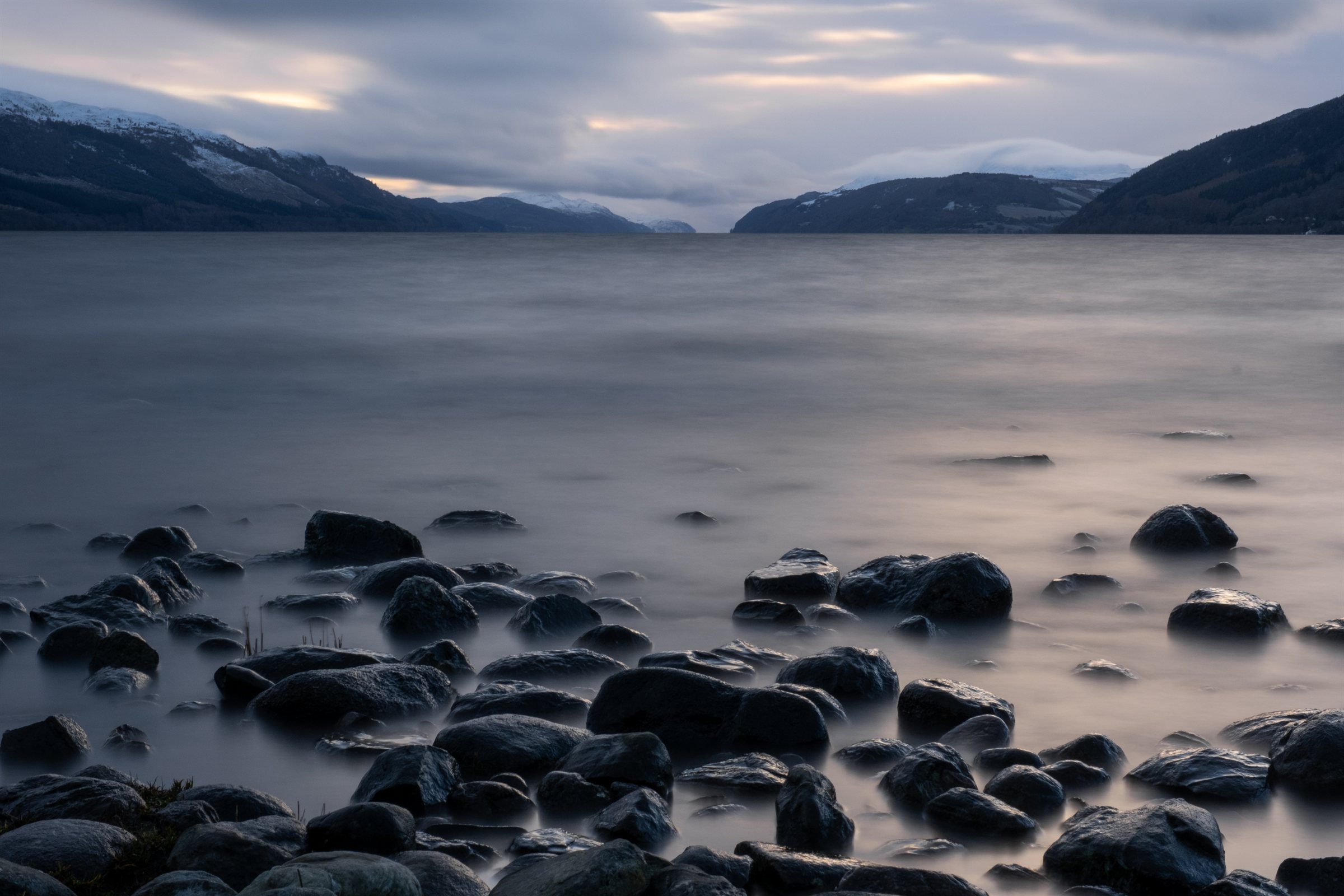 Smooth stones in a misty loch beneath distant hills