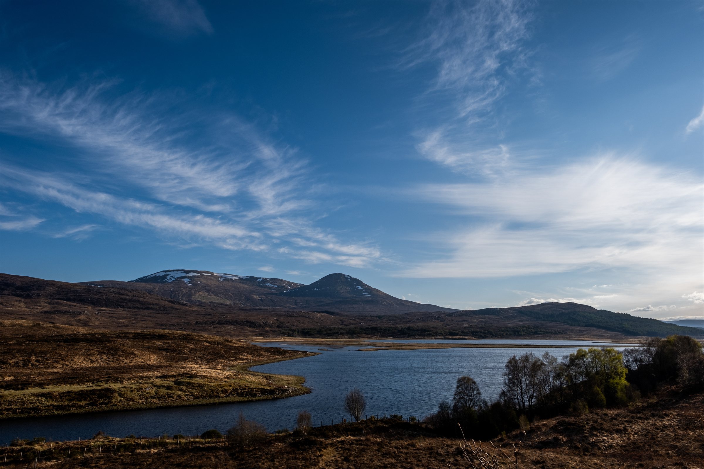 A loch below wispy cloud and a deep blue sky, hills beyond