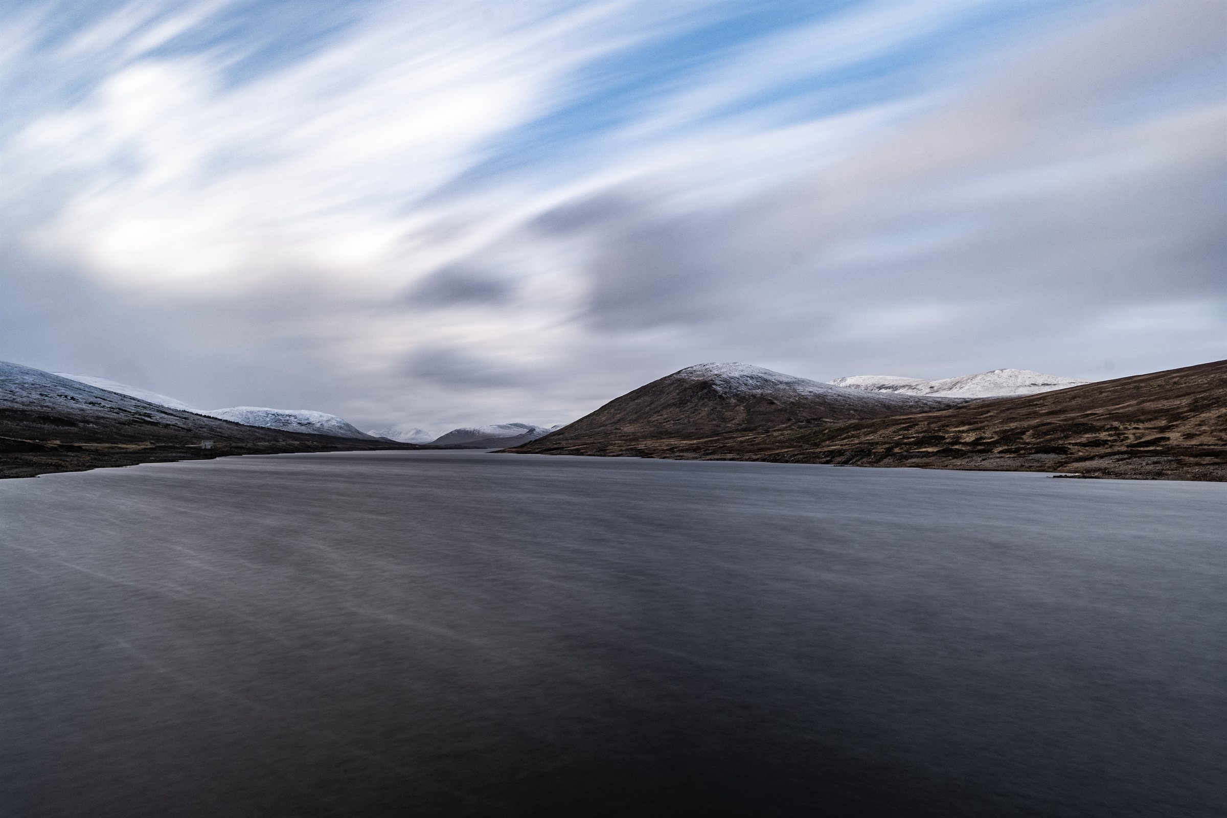 A loch between snow-dusted hills under streaking cloud