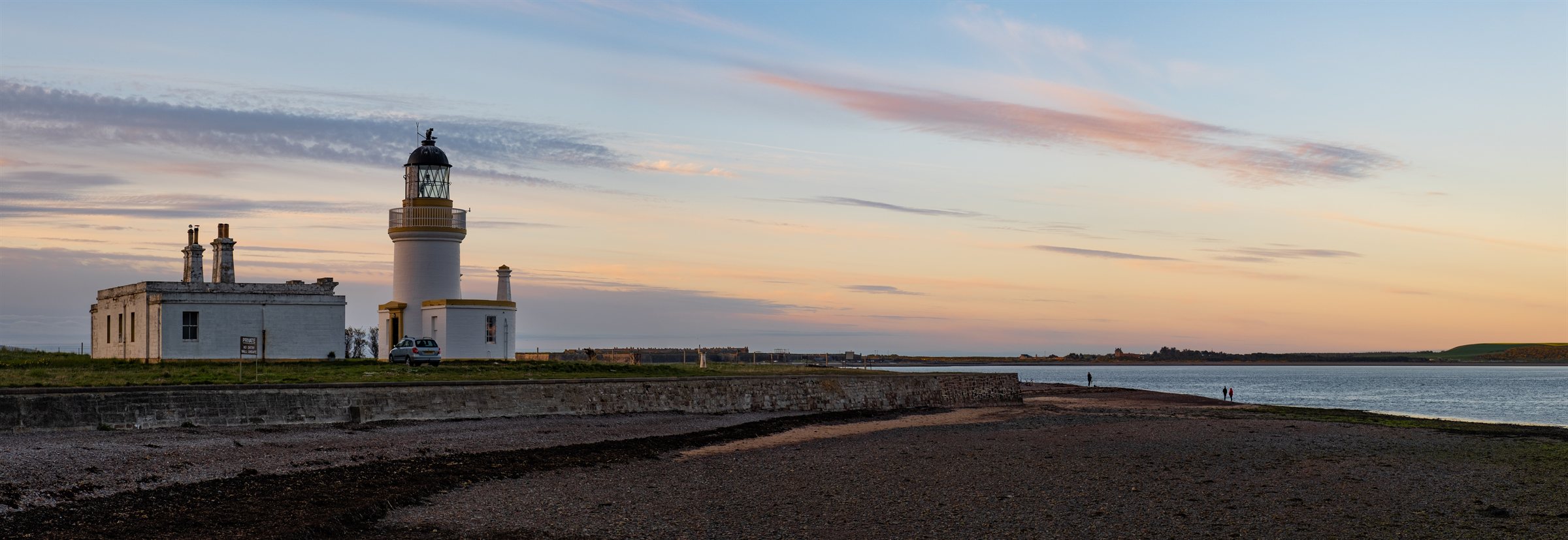 A white lighthouse on a long shore under a pastel evening sky