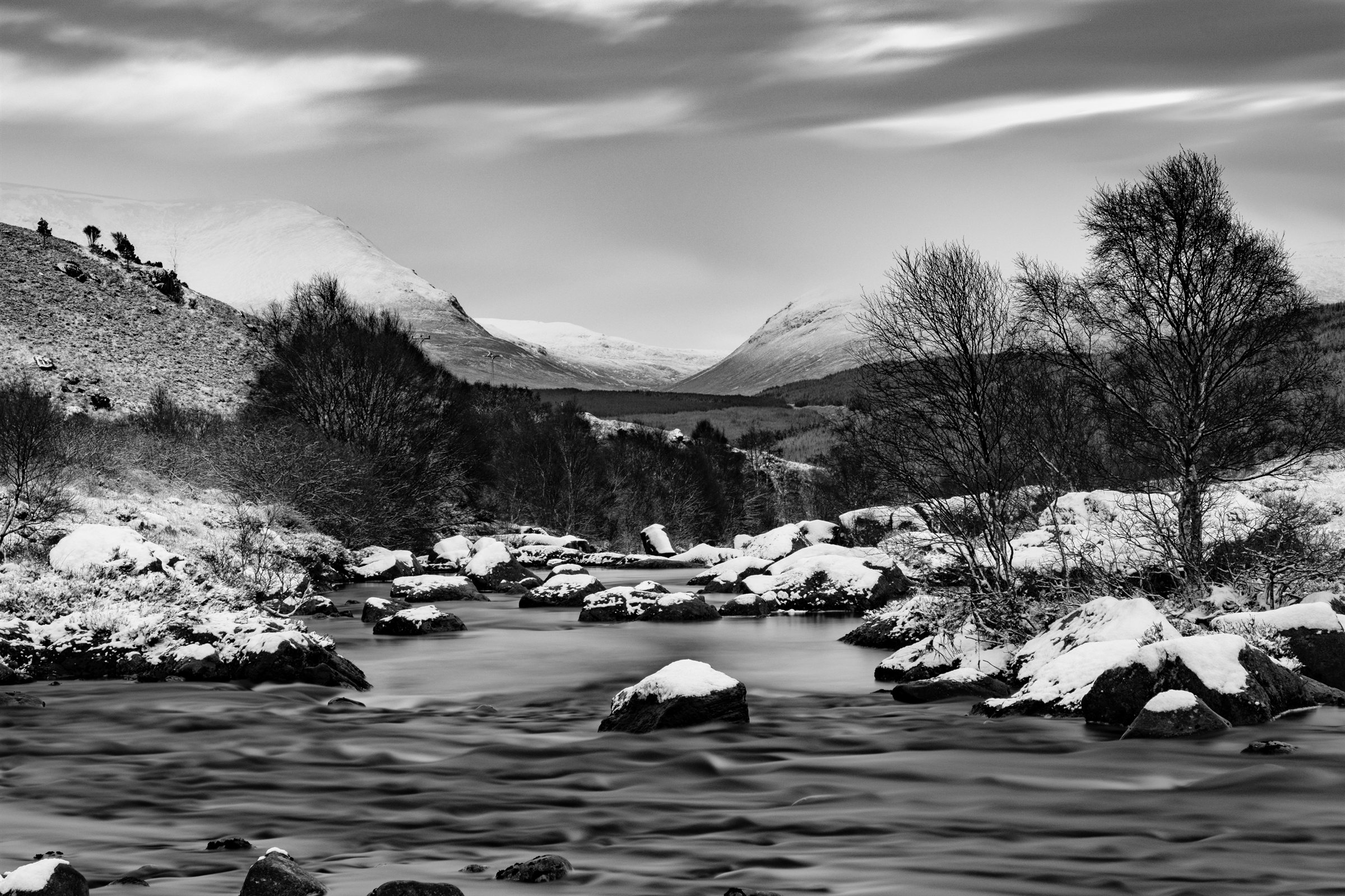 Snow on the boulders of a river below wintry hills
