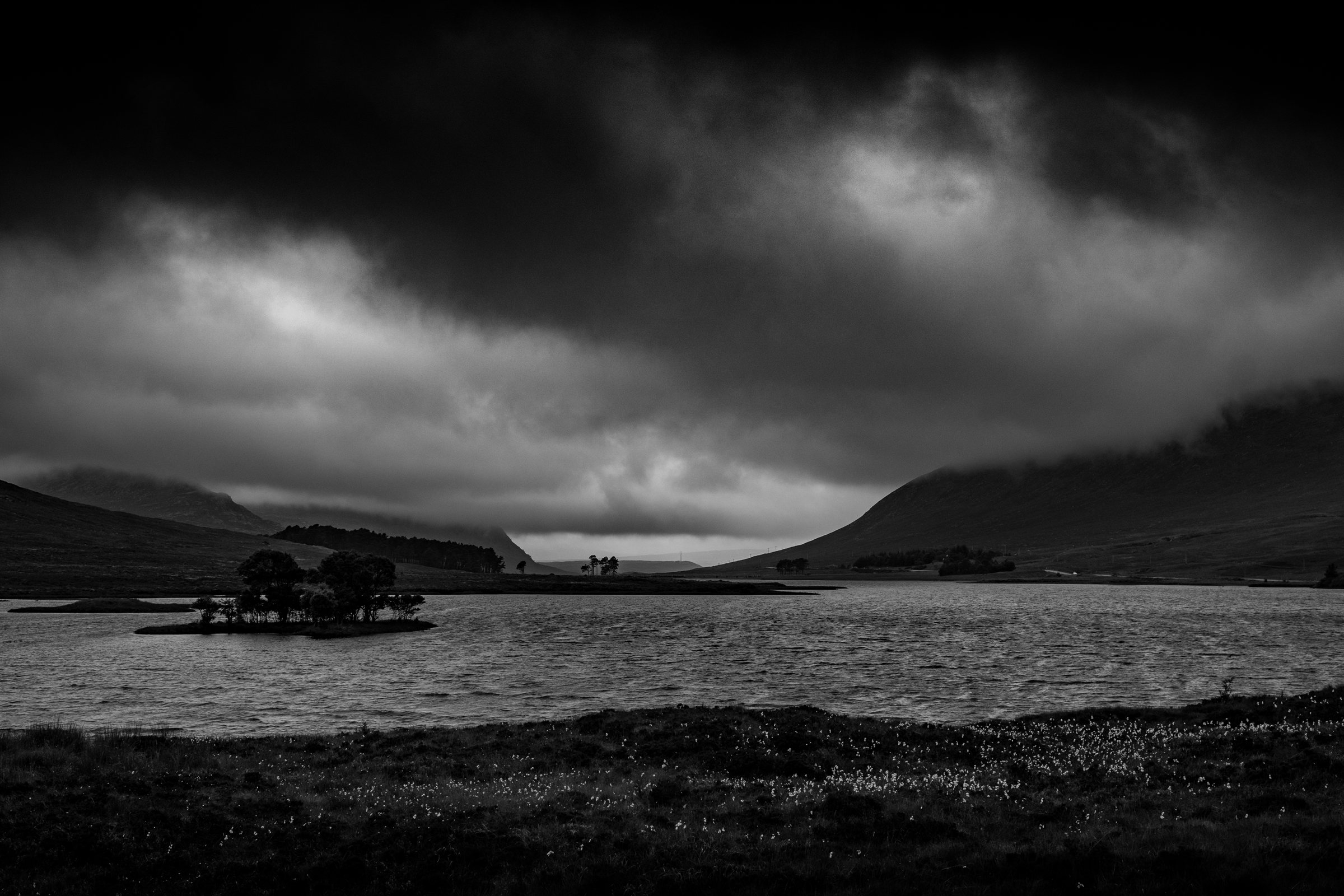 A small wooded island in a loch beneath dark mountains