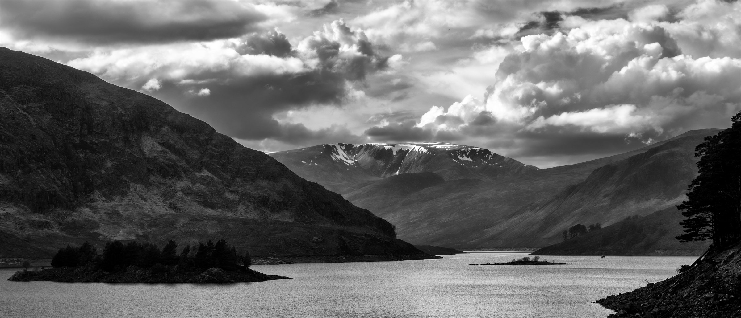 A loch winding between steep mountains under a bright sky