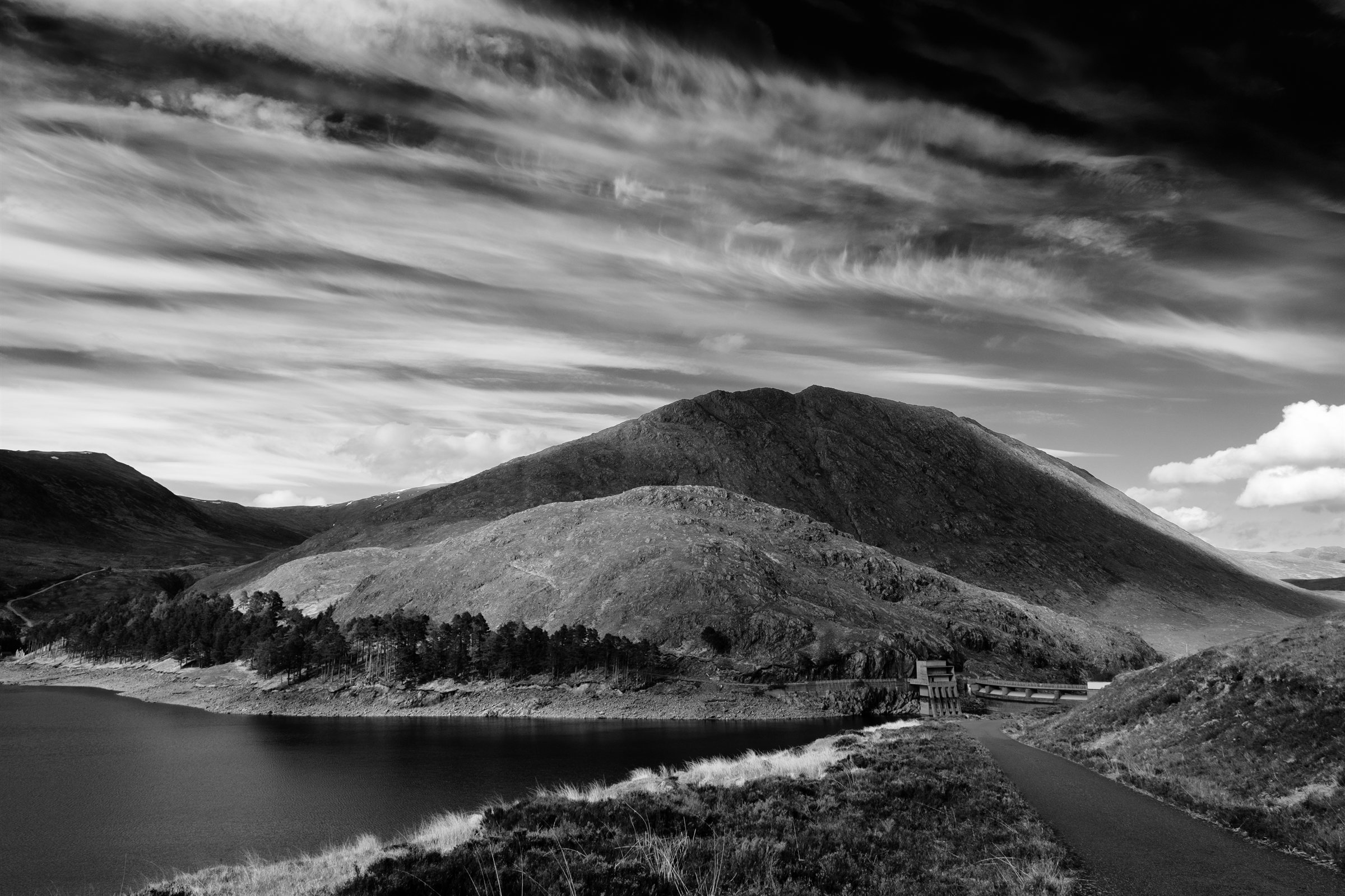 A rounded hill above a loch beneath streaked cloud