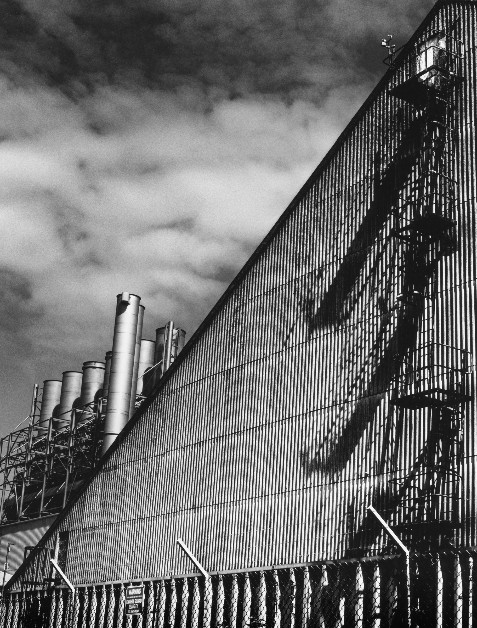 The sloping wall of the maltings throwing the shadow of its ladder, with chimneys beyond