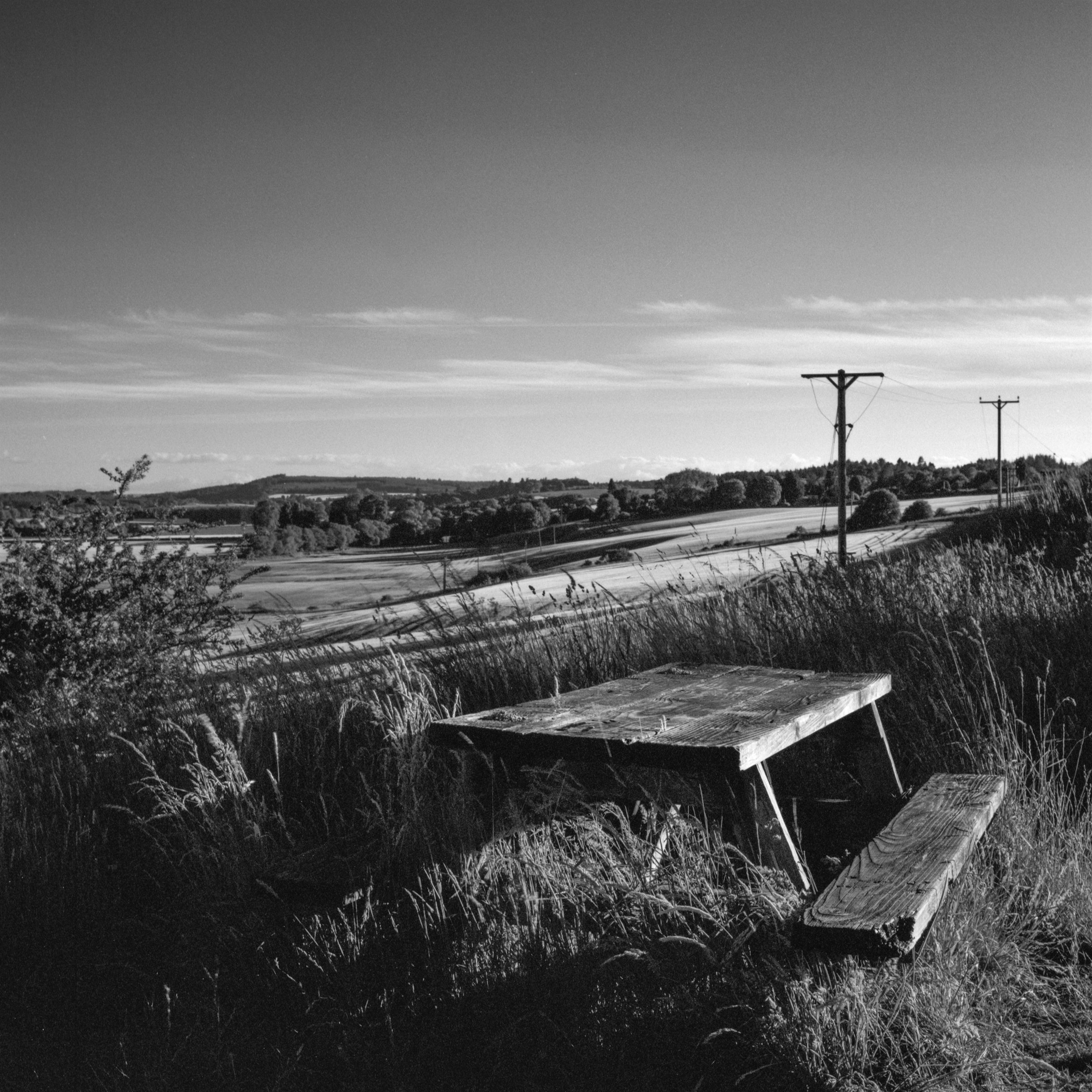An old picnic table in long grass above the fields