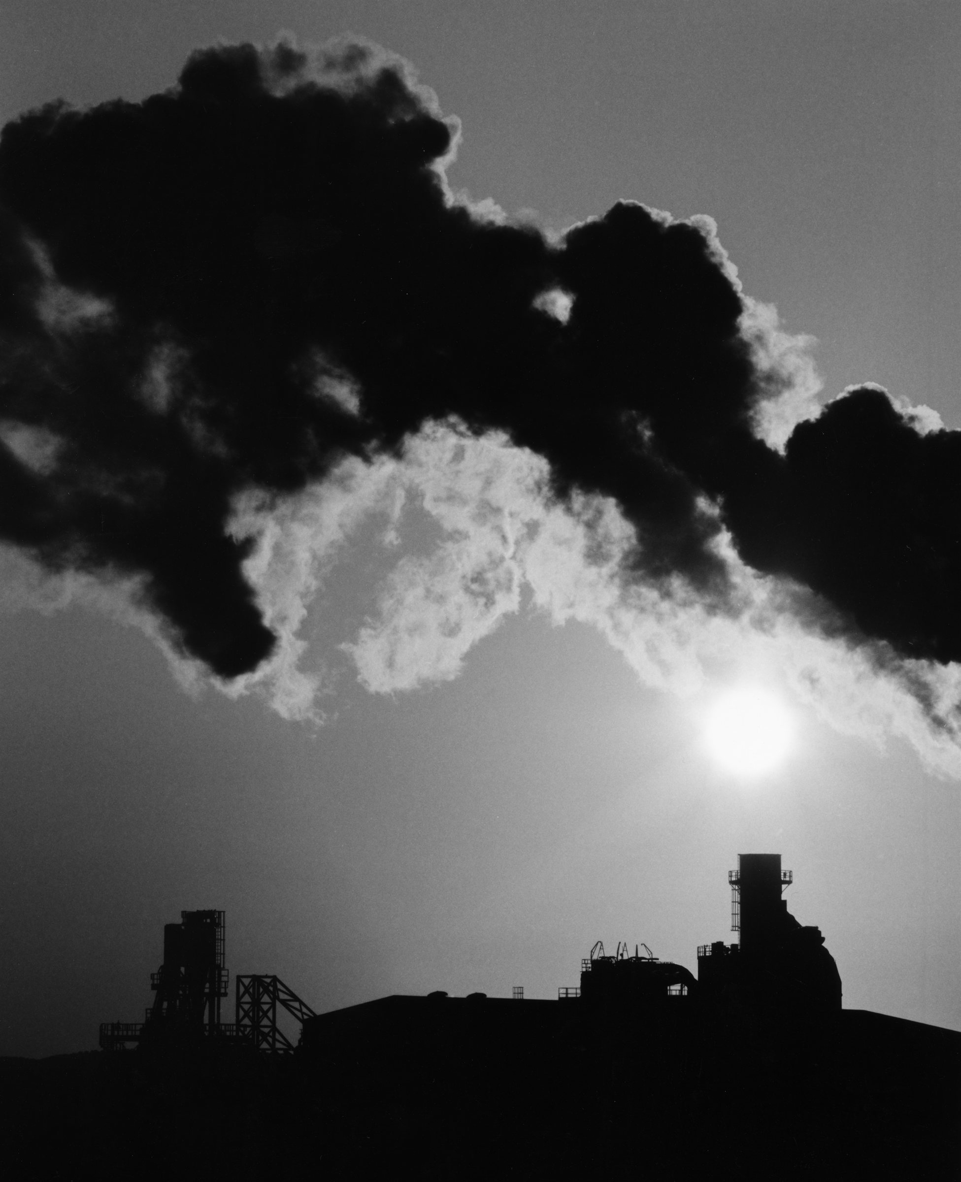 A dark cloud over an industrial skyline and the sun