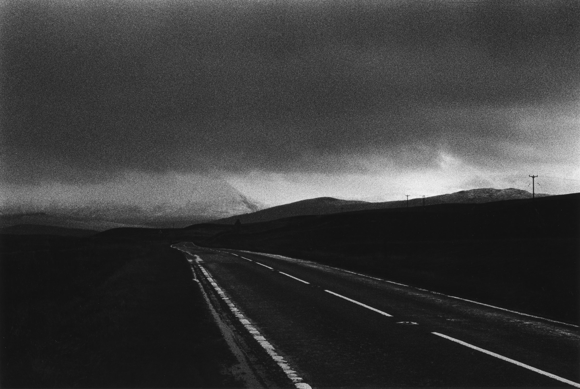 A road running into dark hills under a heavy sky