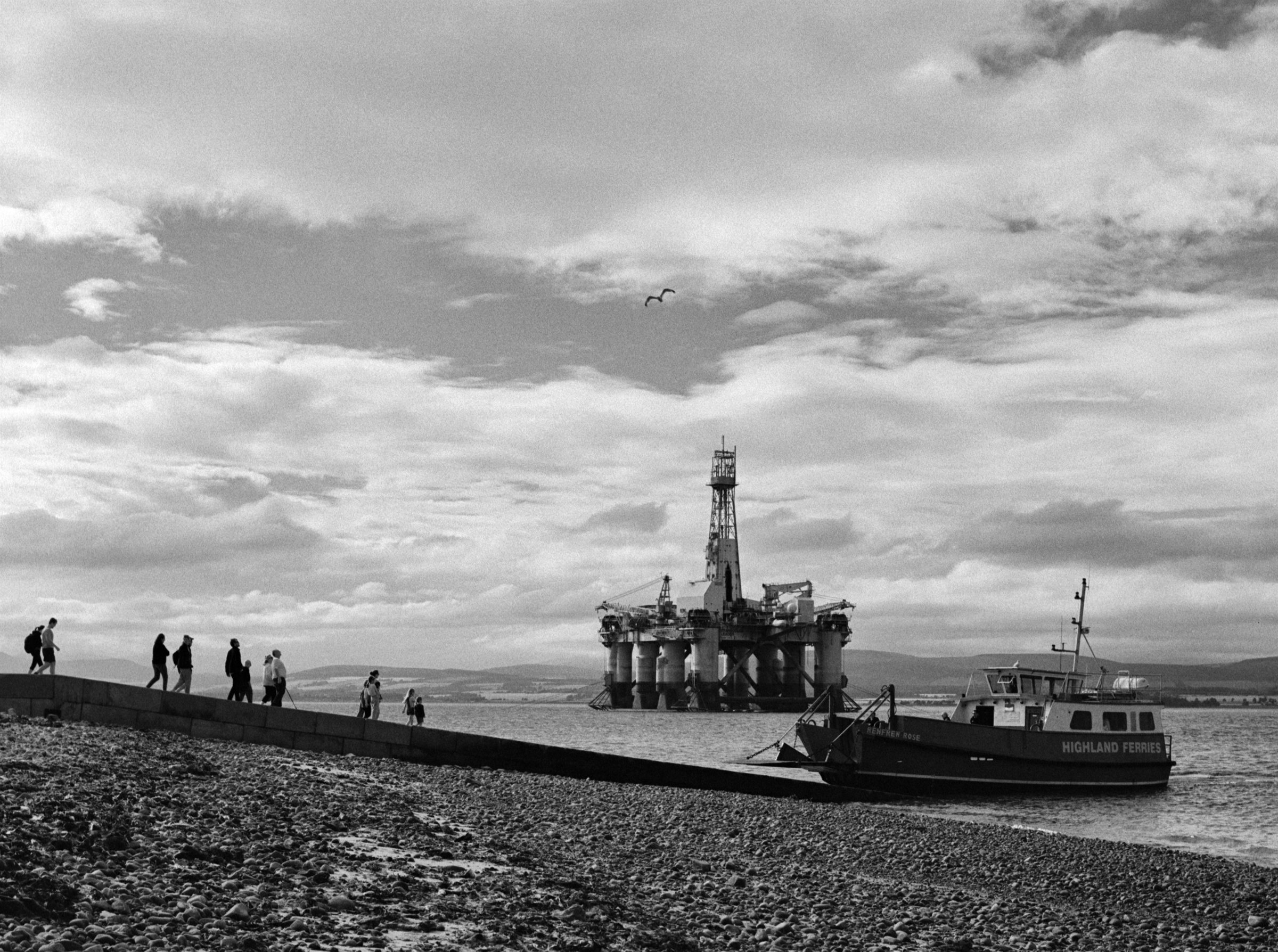 People walking the slipway towards the ferry, an oil rig out in the firth