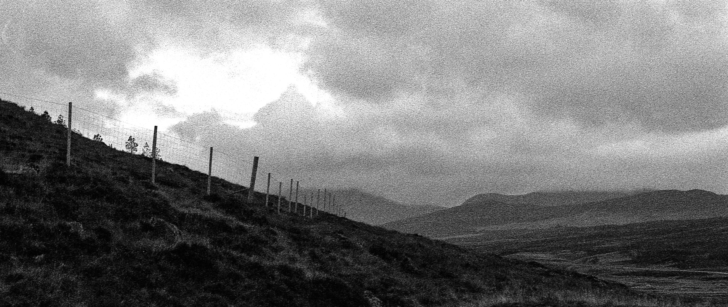 A fence climbing a moorland hill towards misty mountains