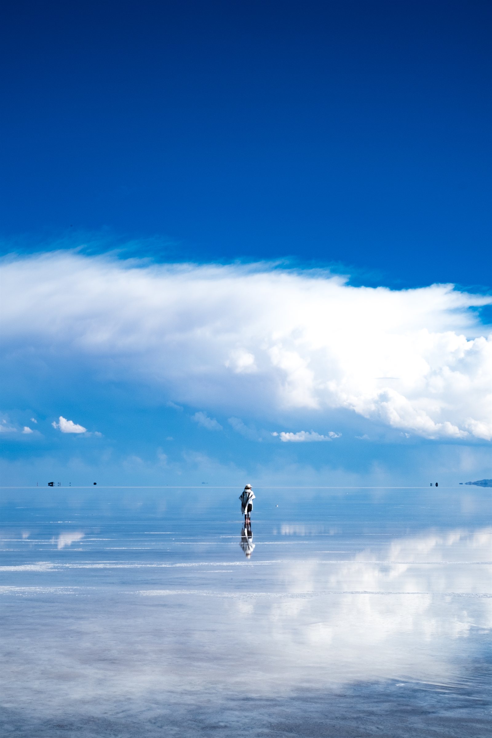 A figure standing on the mirrored salt flats beneath towering cloud