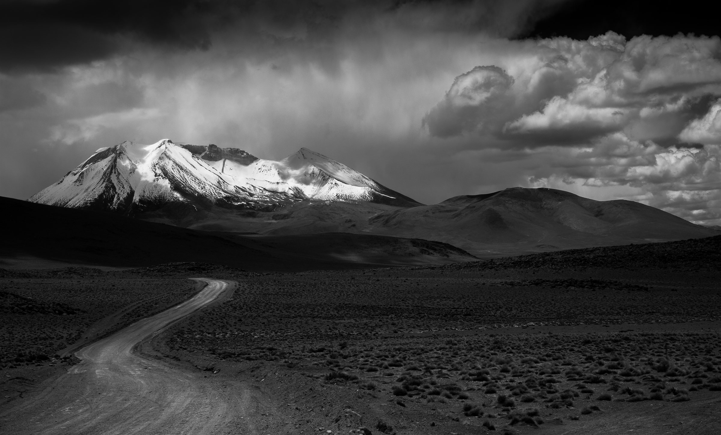 A road winding towards a snow-capped volcano under cloud