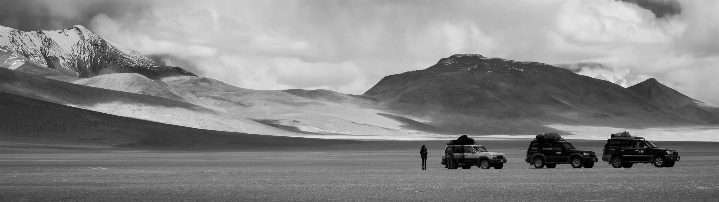 Jeeps on the open plain beneath mountains and cloud
