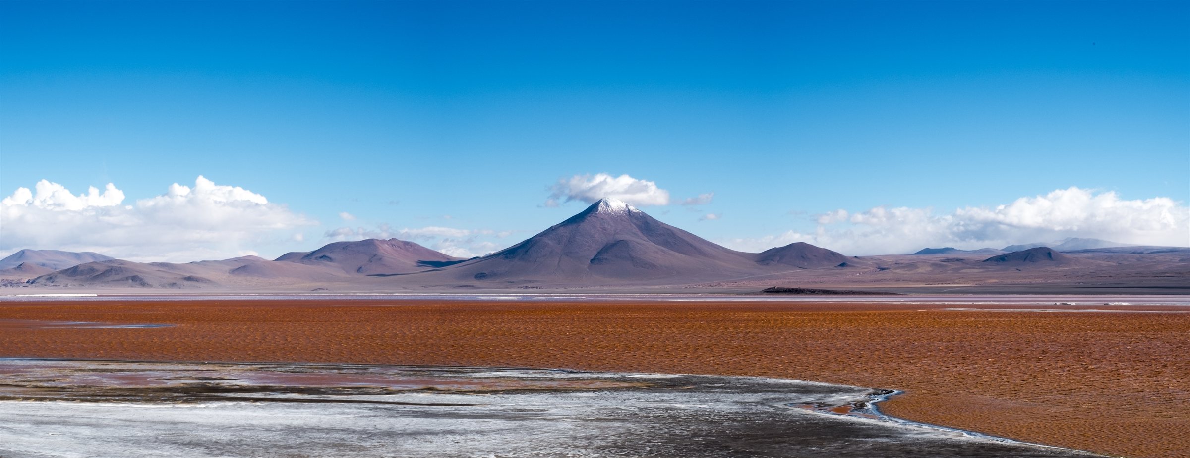 A red lagoon below a volcano and a line of mountains