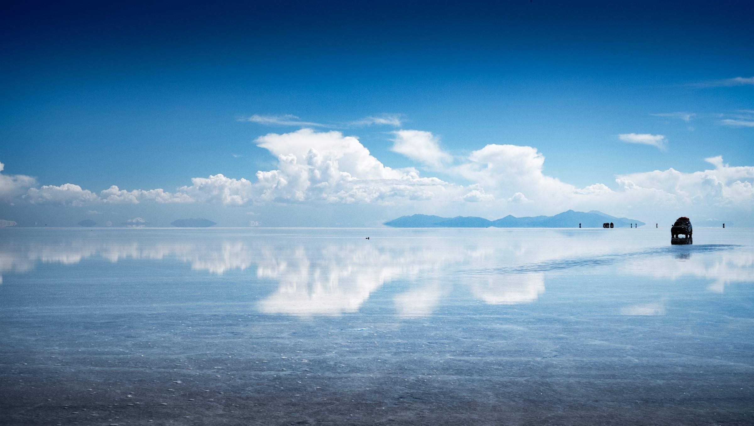 Jeeps mirrored on the wet salt flats under blue sky