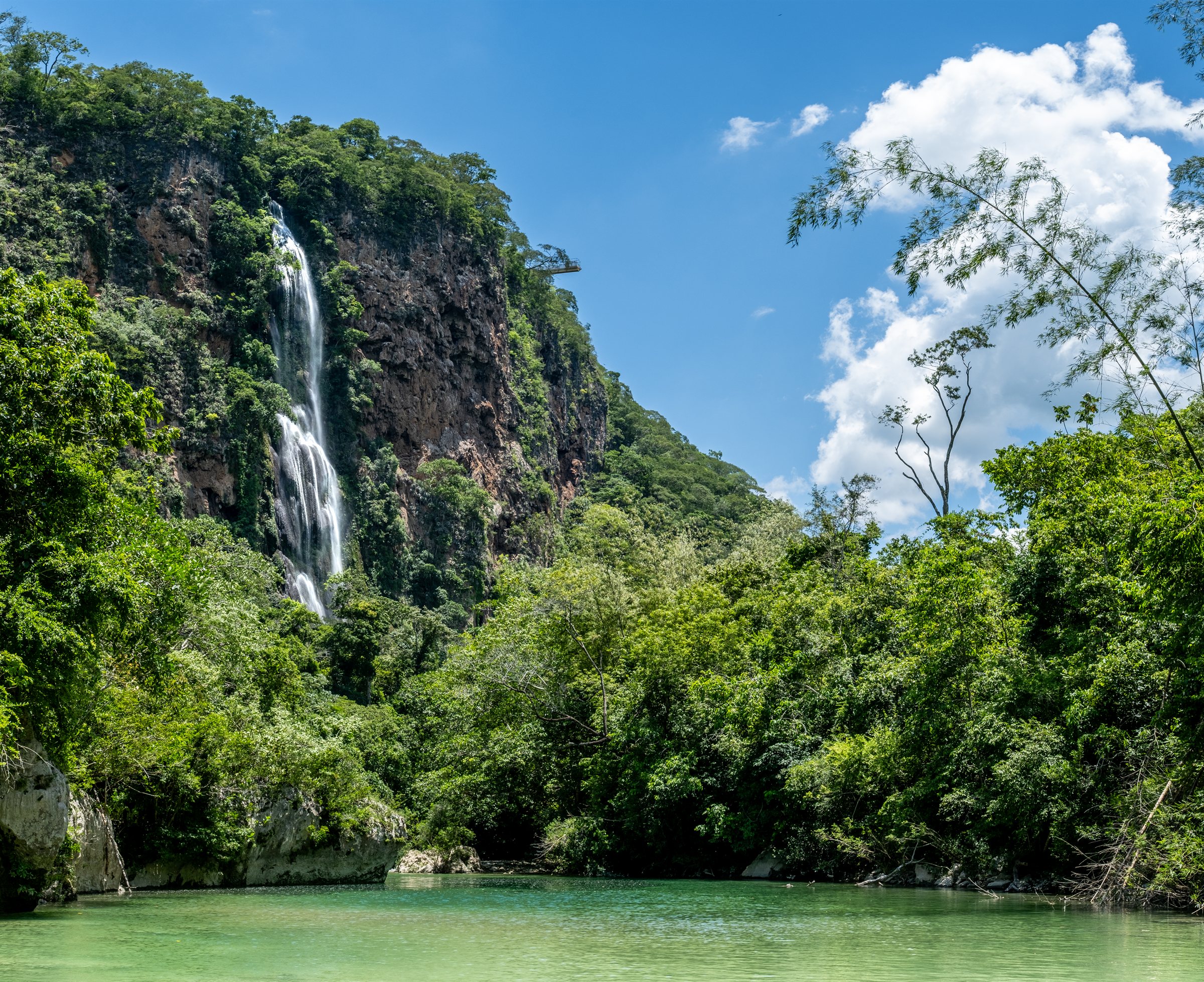 A waterfall falling from a high cliff into a green river
