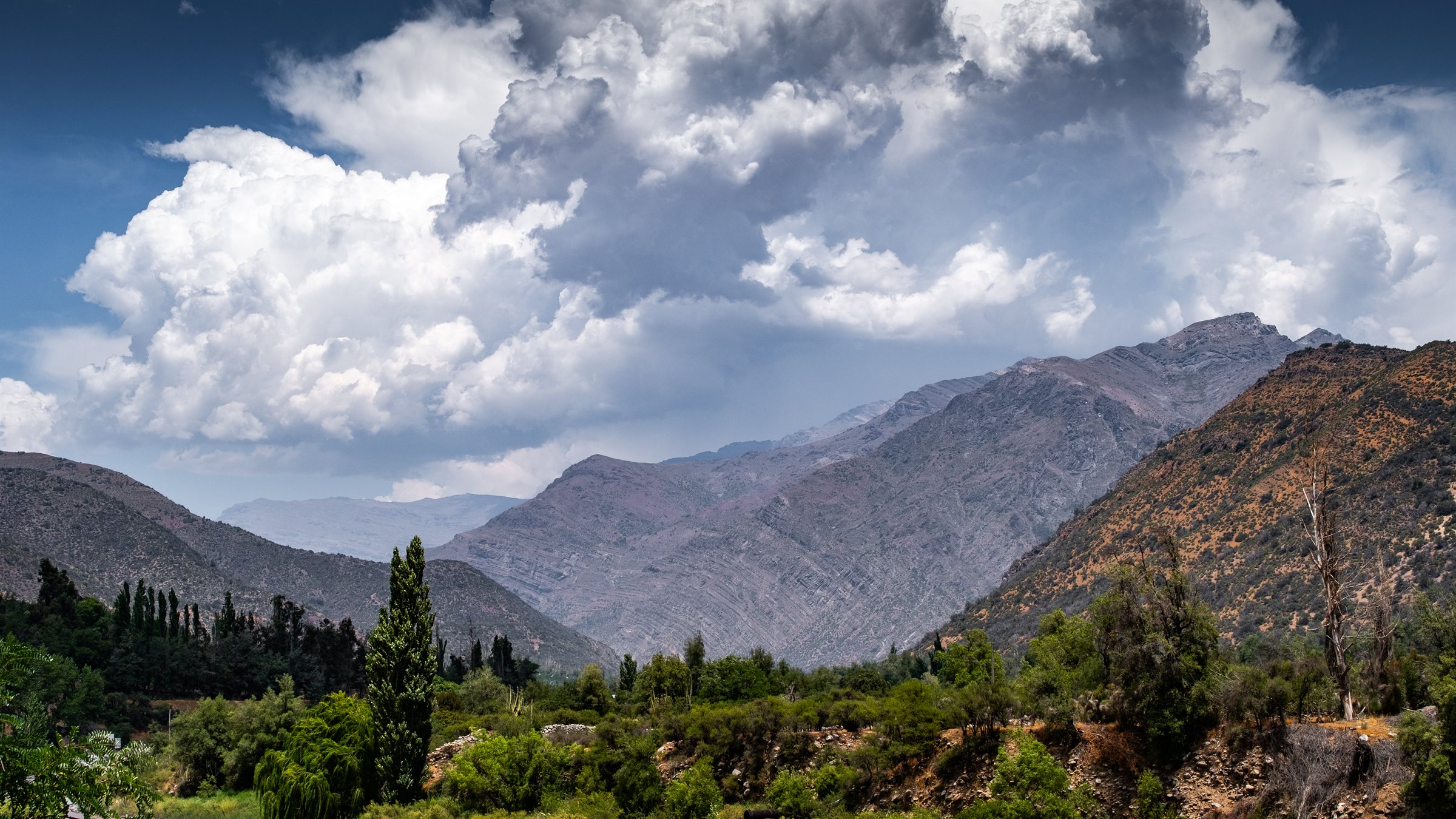 Green valley slopes below jagged Andes peaks and white cloud